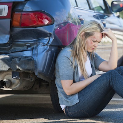 injured person sits on ground beside damaged car