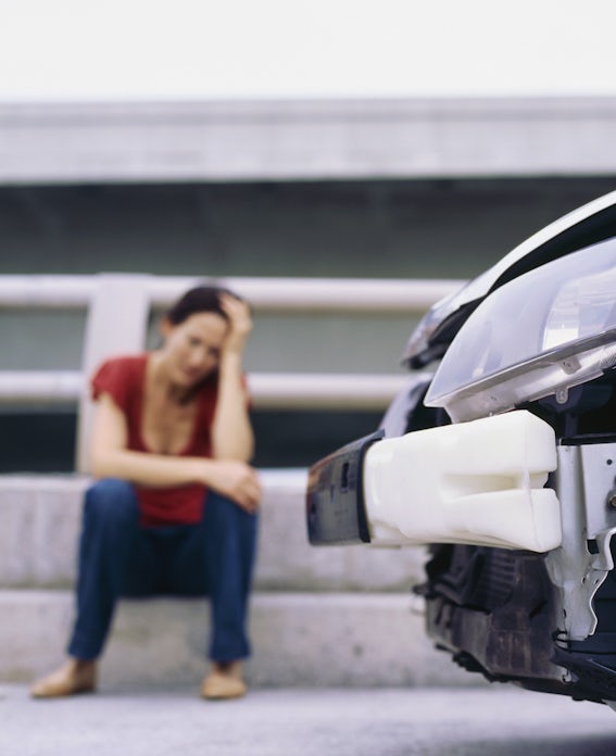 Woman sits on curb next to crashed car
