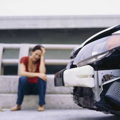 Woman sits on curb next to crashed car
