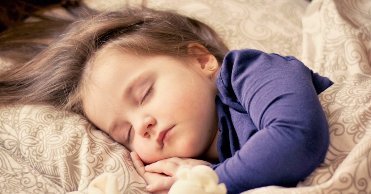 A young child peacefully sleeping on a patterned bed with hands tucked under the chin, symbolizing restful sleep and relief from bedwetting.