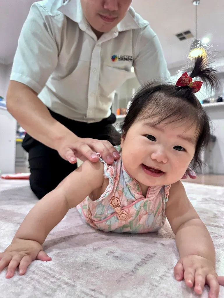 Baby girl smiling while a chiropractor gently checks her shoulders during a developmental assessment