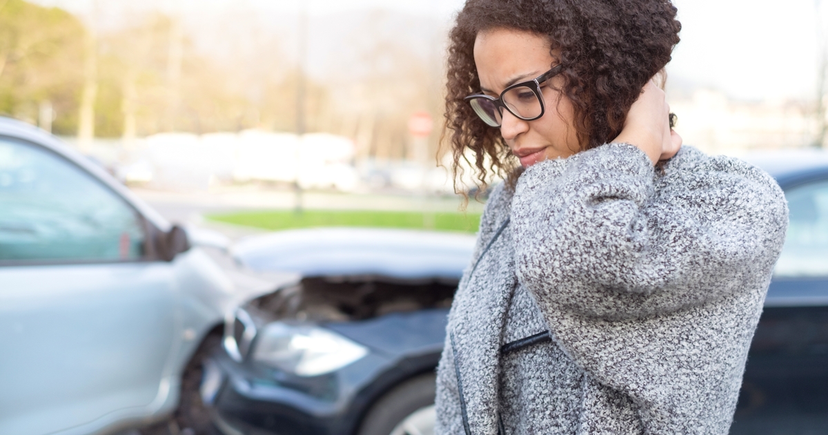 The image shows a person with curly hair and glasses, looking distressed near two cars involved in an accident.