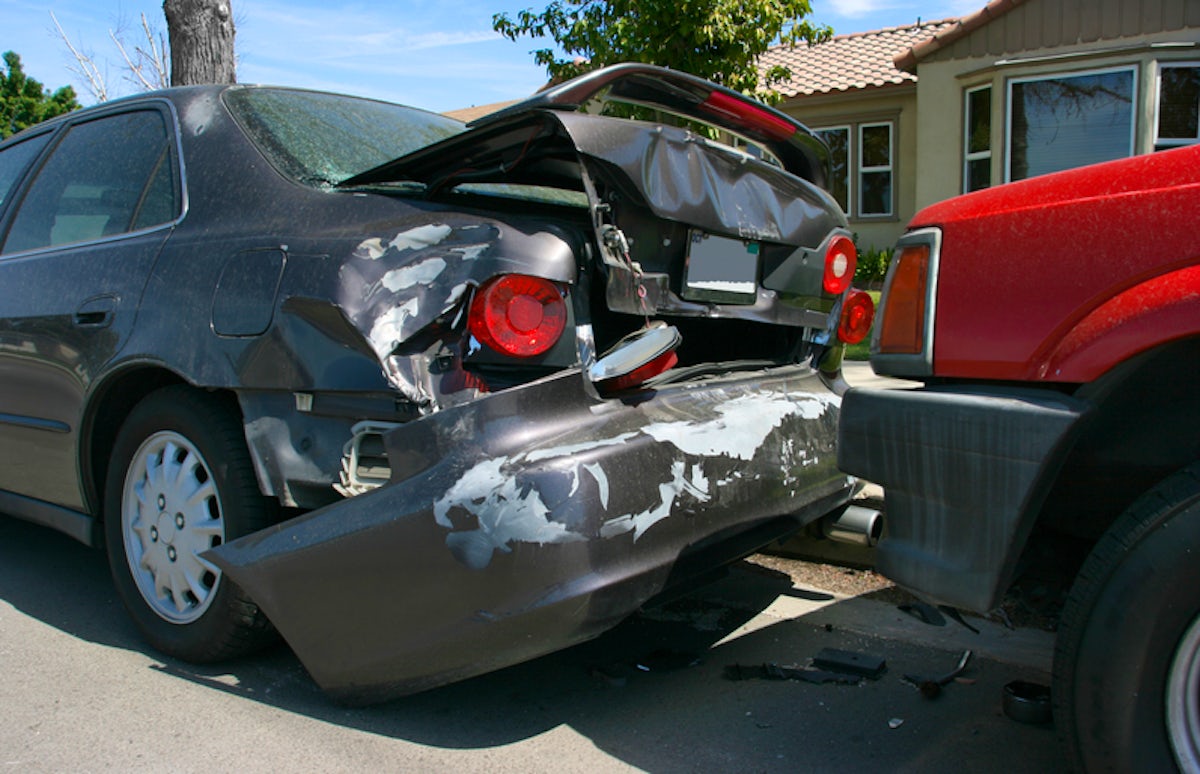 The image shows two parked cars, one with significant rear damage due to a collision, and the other with visible impact on the bumper.