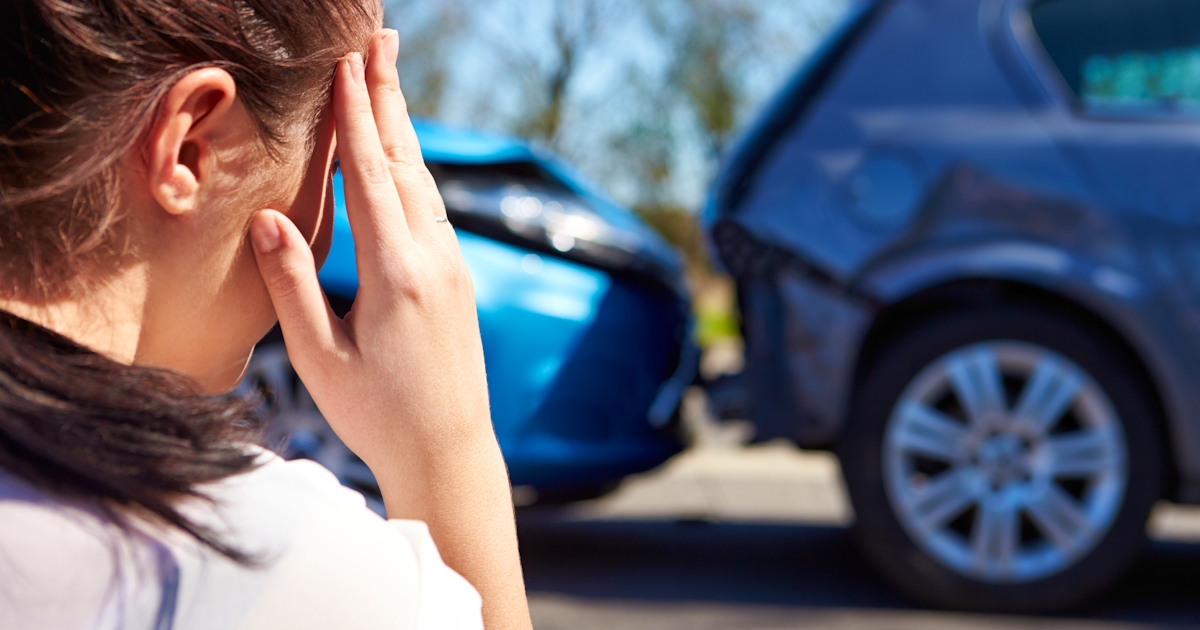 The image shows a person with their hand on their forehead, looking distressed near two cars that have been involved in a collision.