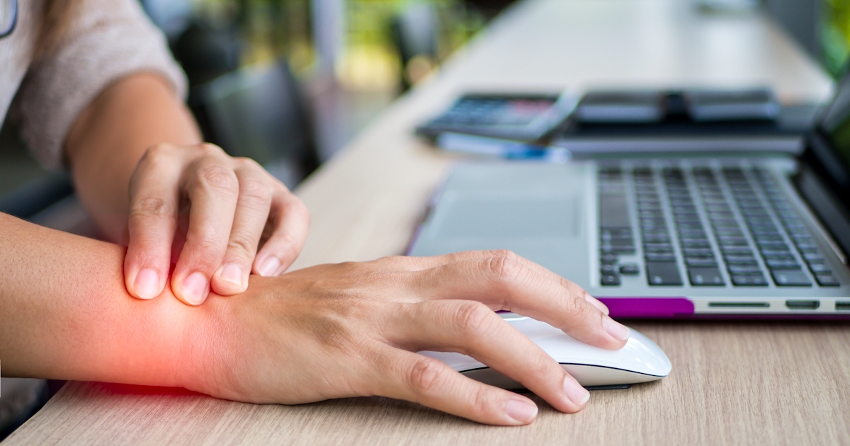 person grabs wrist in pain while using computer