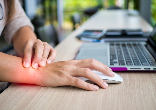 person grabs wrist in pain while using computer