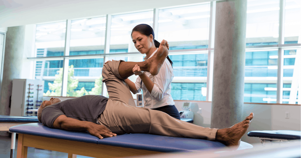 Therapist helps mature man carefully bend leg afte