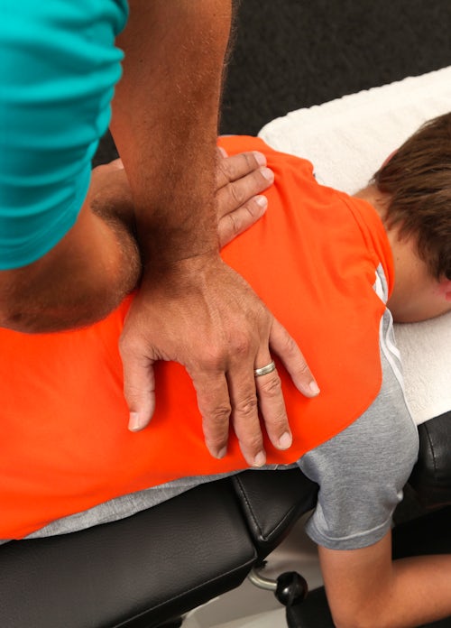 The image shows a person receiving a massage or chiropractic adjustment while lying face down on a treatment table.