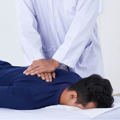 A healthcare professional performs a spinal adjustment on a patient lying face down on a treatment table in a clinical setting.