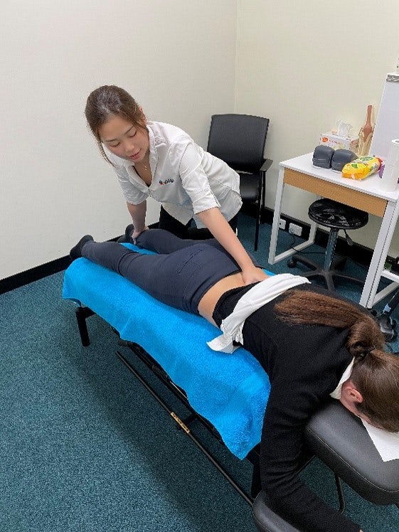 Chiropractor performing flexion-distraction therapy on a patient's lower back while they lie face down on a treatment table.