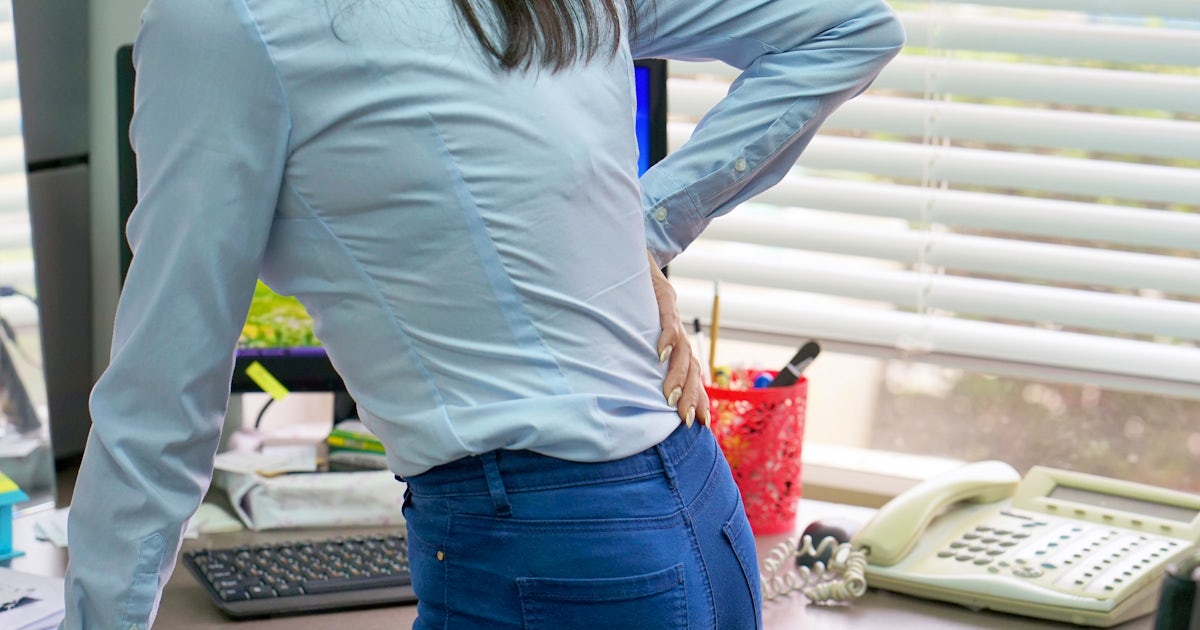 close up from the back of female office worker standing at desk holding low back pain