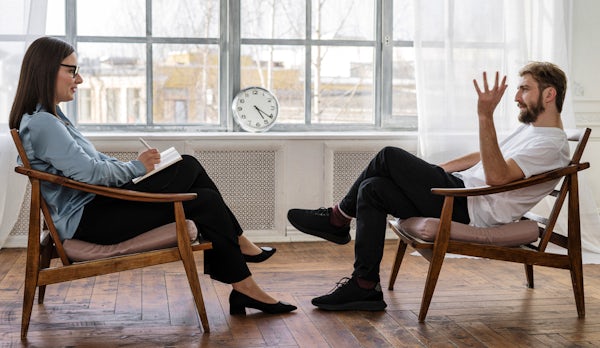 A counselor and client sit in chairs facing each other
