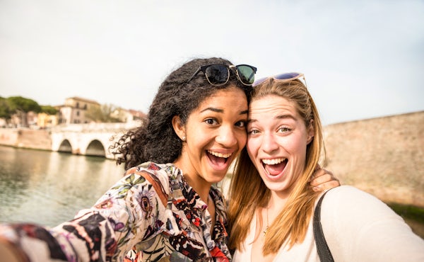 Happy multiracial girlfriends taking selfie and ha