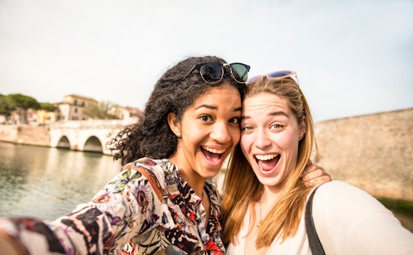 Happy multiracial girlfriends taking selfie and ha