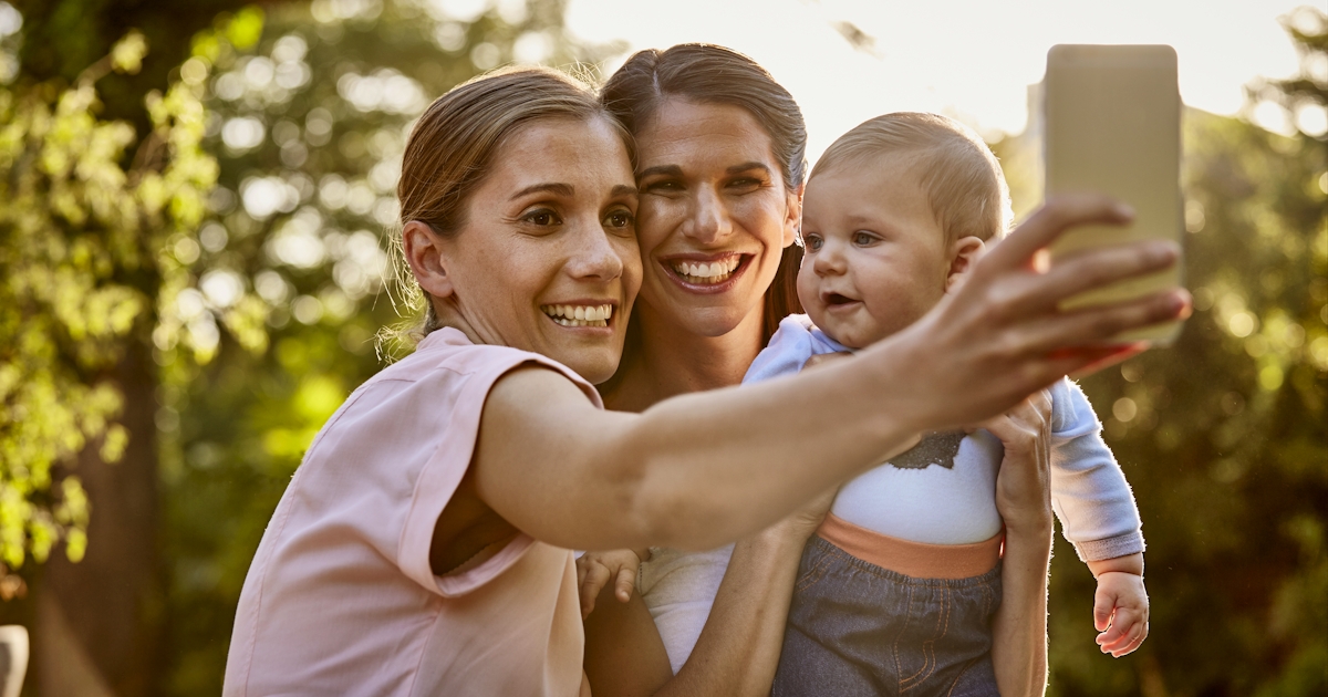 Lesbian couple with baby taking selfie in park