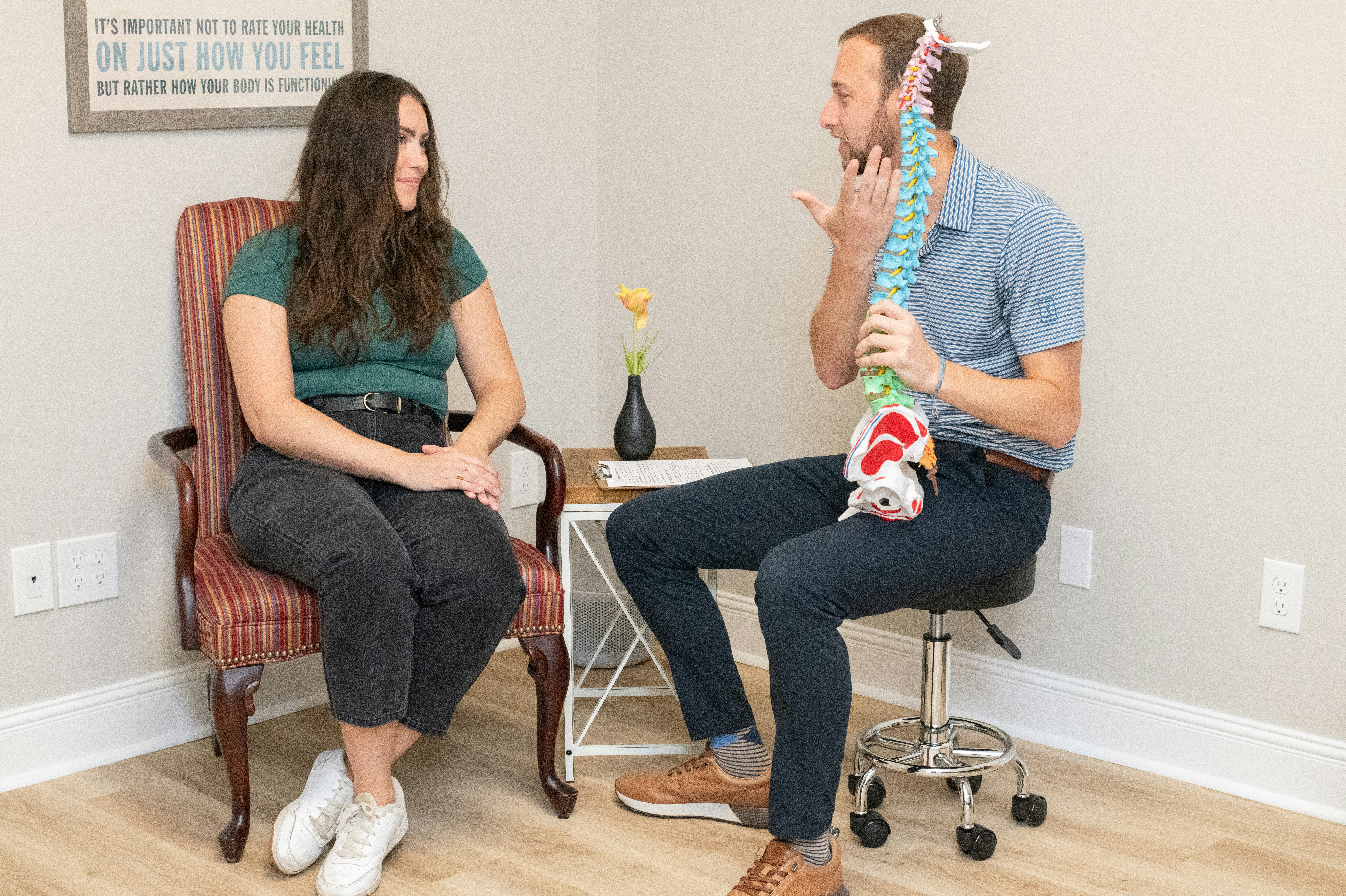 Dr. Hyde and Dr. Simon roleplaying as doctor and patient, discussing chiropractic care while Dr. Hyde hold a sculpture of a spine.
