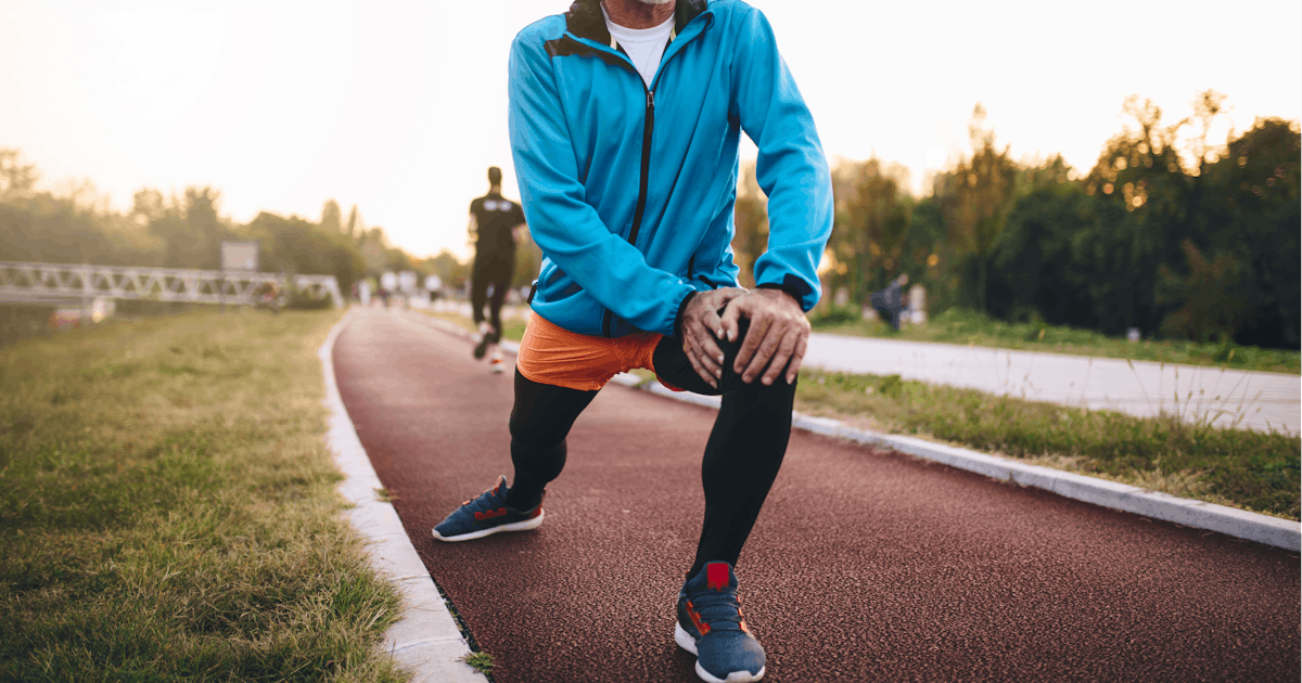 Senior man stretching while jogging on a track