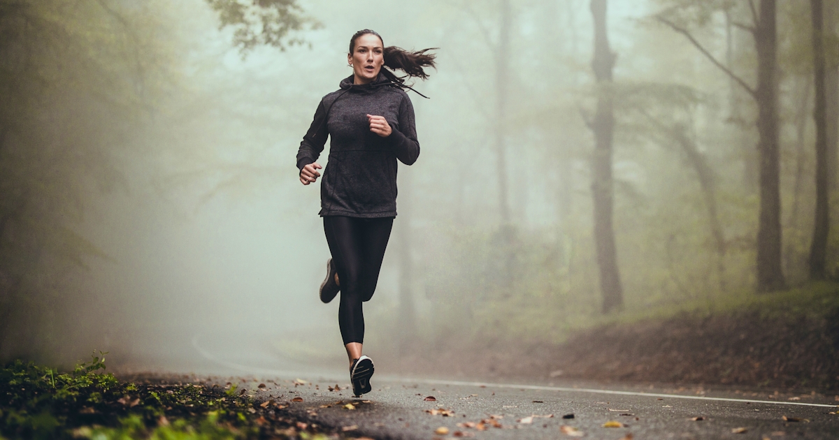 Young athletic woman jogging on the road in foggy 