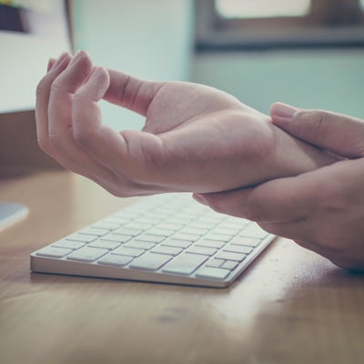 up close white hands at a keyboard left hand touching right wrist