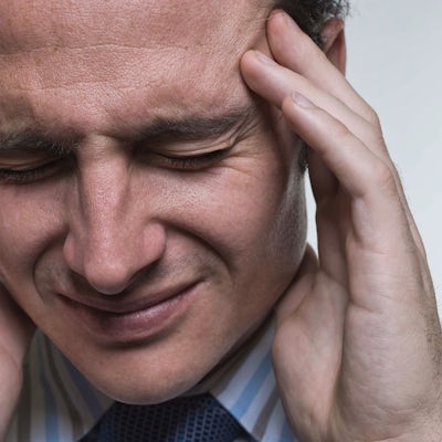 A man in a striped shirt and tie is holding his head with both hands, appearing distressed or in pain. His expression suggests discomfort.