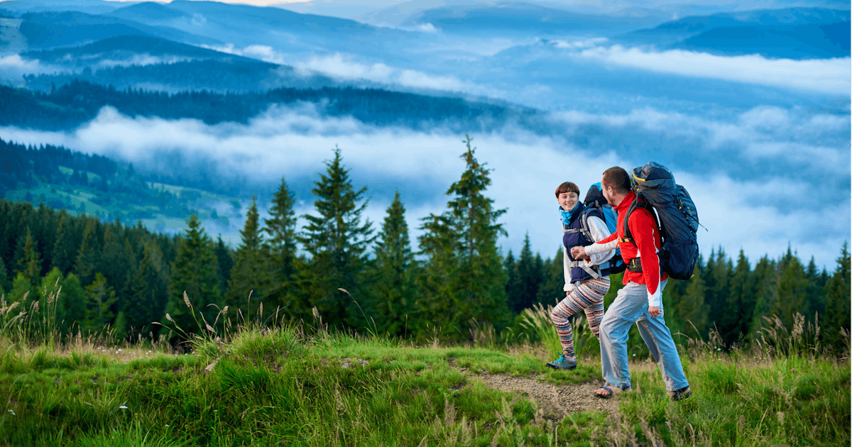 Two hikers are walking on a trail surrounded by lush greenery and misty mountains, enjoying the scenic view.