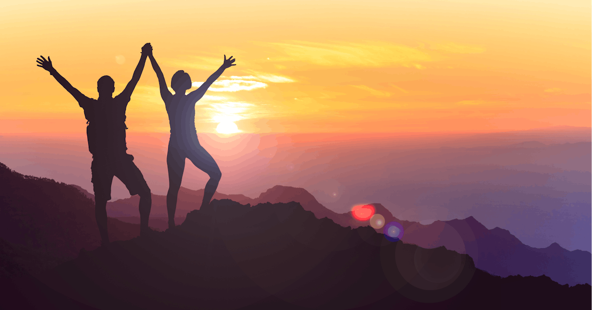The image depicts two people silhouetted on a mountain peak, raising their arms in celebration against a vibrant sunset sky.