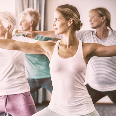 white female yoga instructor with elderly people standing exercising