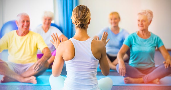 female yoga instructor with elderly people seated on mats