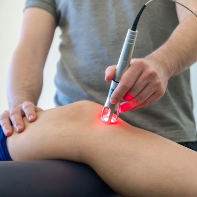up close white male leg laser therapy on knee glowing red male chiropractor doctor