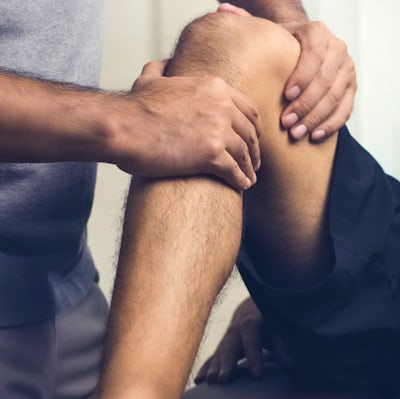 Therapist treating injured knee of athlete male pa