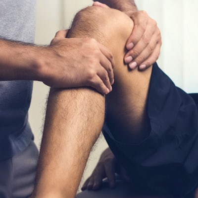 Therapist treating injured knee of athlete male pa