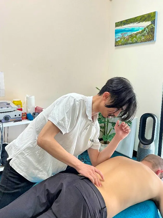 Massage therapist performing deep tissue massage on a male patient's lower back to alleviate muscle tightness and discomfort.