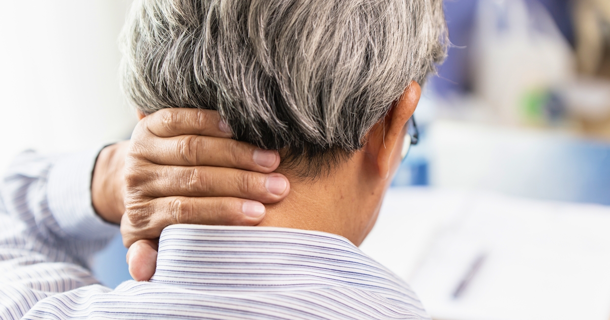 An older individual with gray hair is seen from behind, gently holding their neck, possibly indicating discomfort or stretching.
