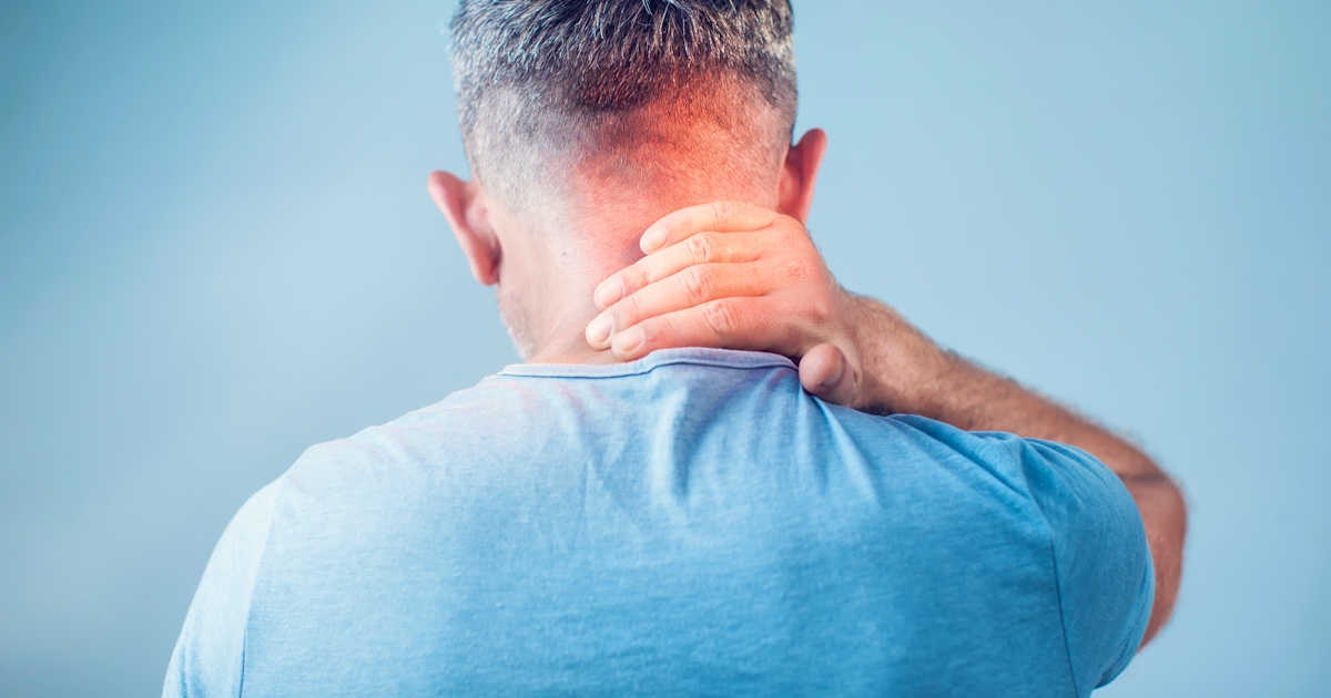 A person with short hair is touching the back of their neck, appearing to experience discomfort or tension. The background is a soft, blurred blue.