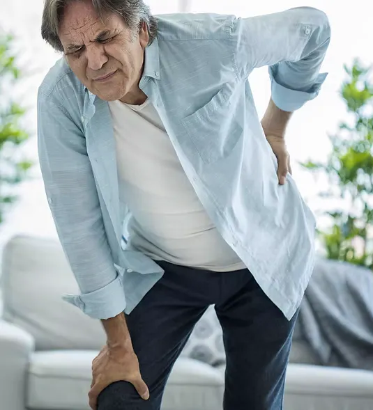 Older man holding his lower back and knee with pain and reduced mobility associated with lumbar spinal stenosis