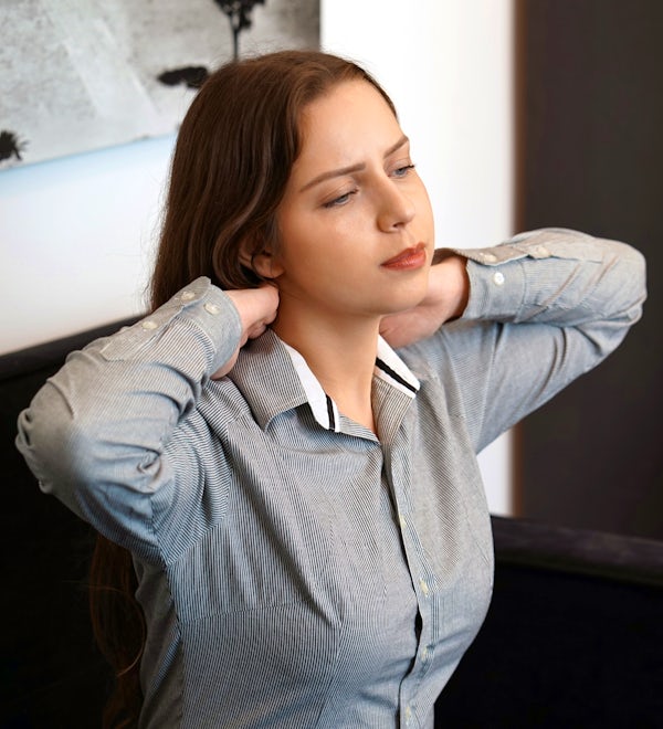 upper half seated young brunette female holding back of neck in pain