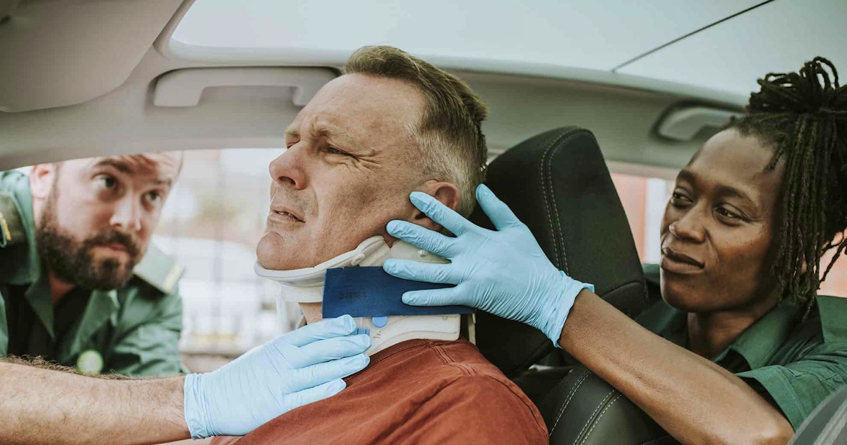 Paramedics fitting a neck brace on a man in a car after a car accident addressing potential whiplash injury and cervical spine support