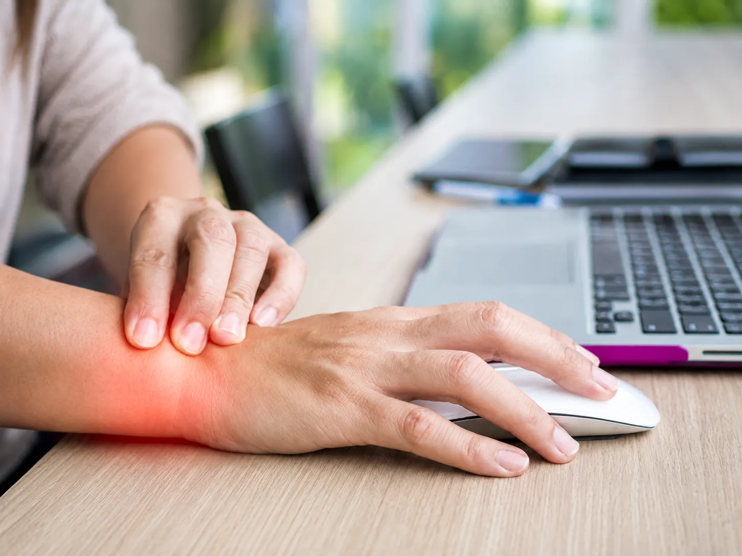 Person holding their wrist while using a computer mouse with repetitive strain injury and wrist pain