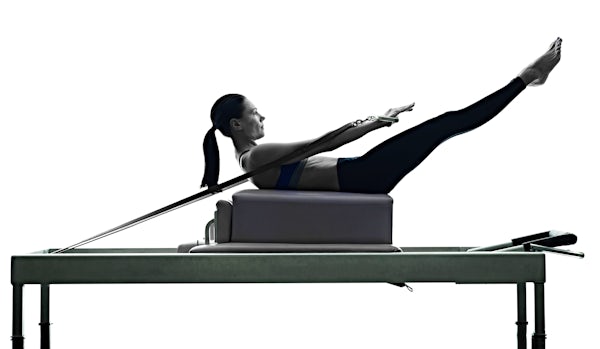 The image shows a person performing an exercise on a Pilates reformer, engaging in a core-strengthening position with extended legs.