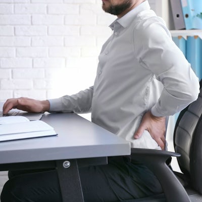 white male sitting at desk left side view with left arm holding low back pain