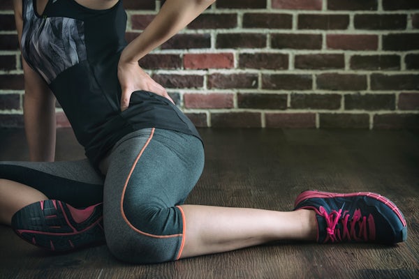 up close female athlete sitting down indoors stretching holding low back pain