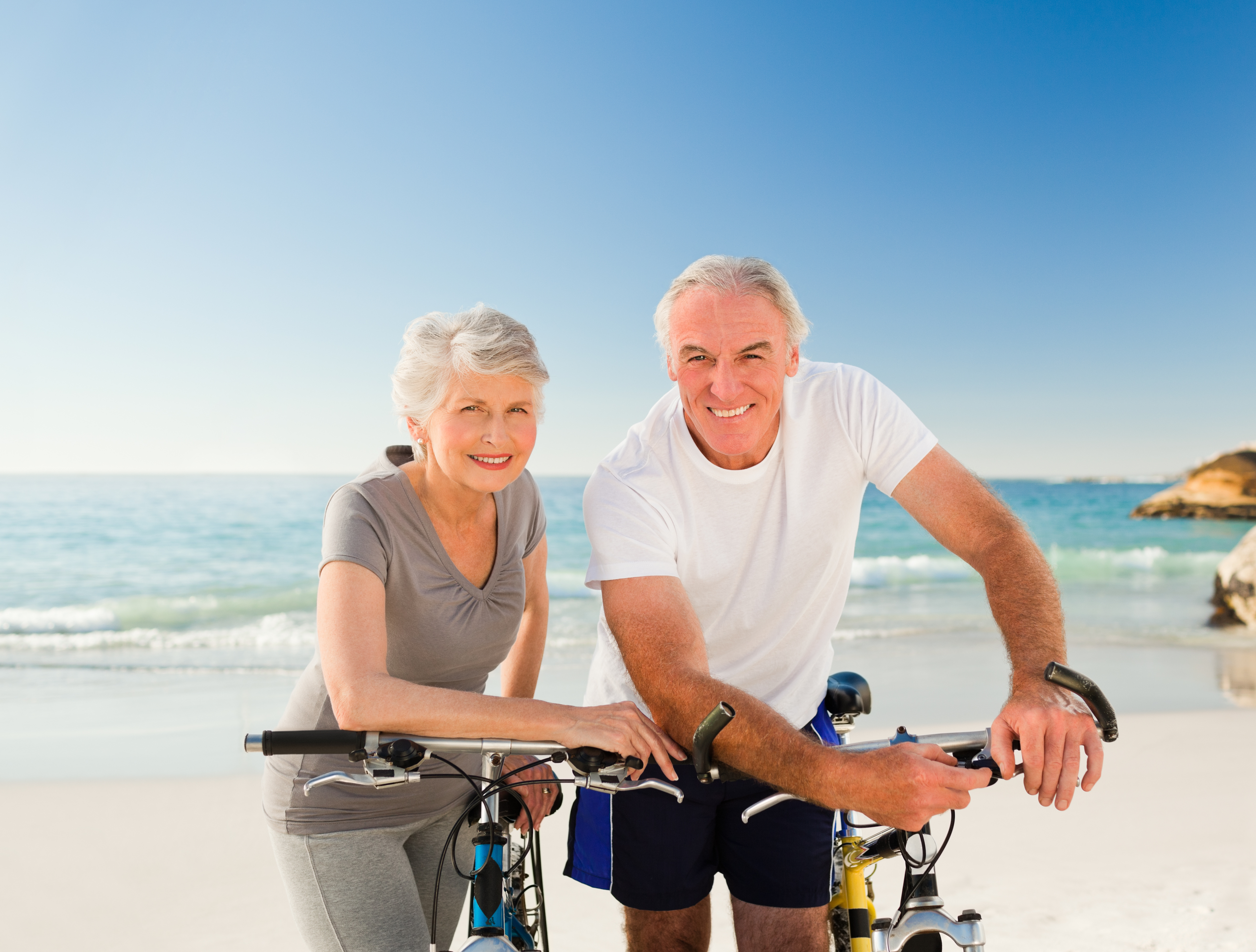 happy senior white couple at the beach on their bikes