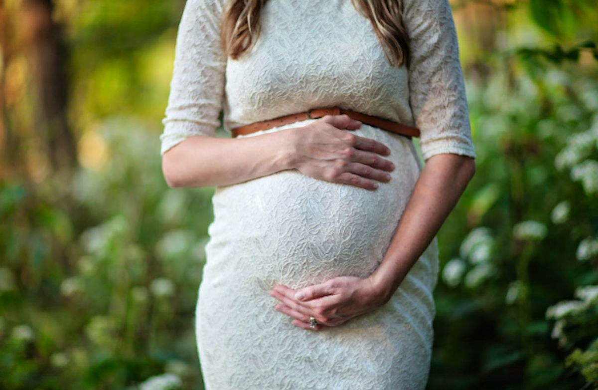 Pregnant woman in white lace dress with hands on belly