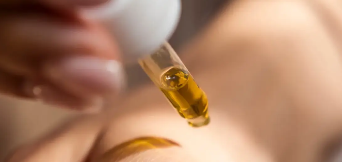 Castor oil being applied with a dropper near the eyebrow area