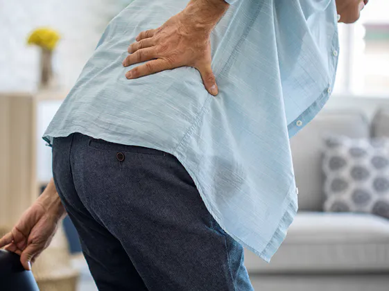 Older adult holding the lower back with pain and stiffness associated with spinal degeneration