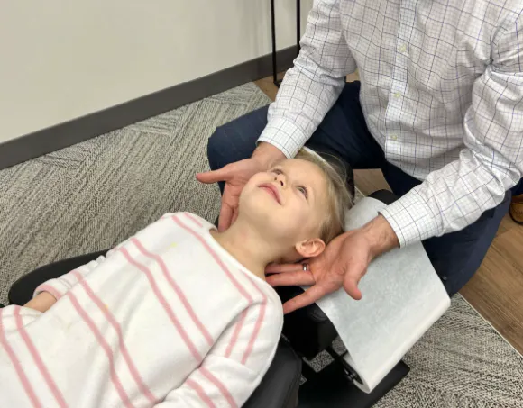 Child receiving a gentle neck and spinal assessment in a clinical setting