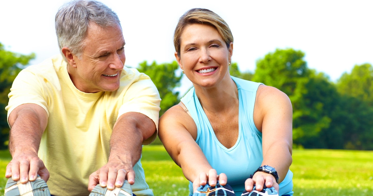 couple of happy seniors outside sitting on grass stretching green beautiful