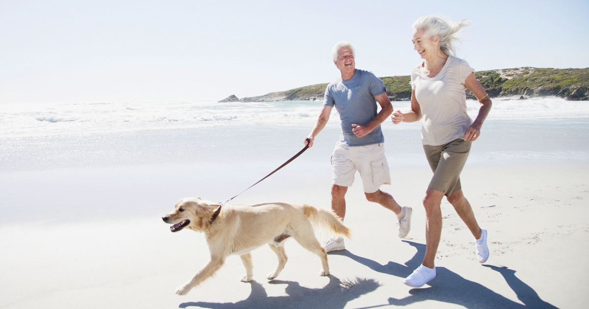 Senior couple running on beach with dog