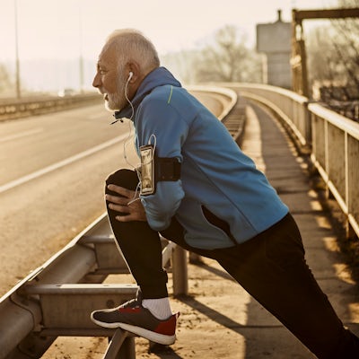 Senior man warming up for jogging on a city bridge