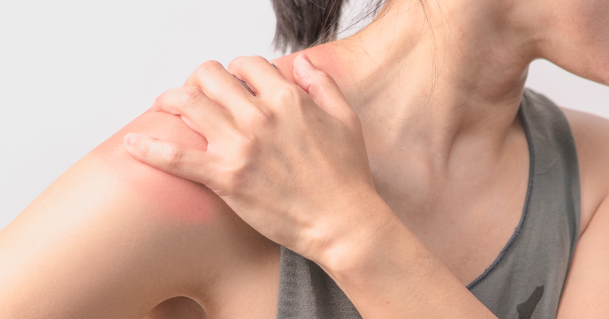 The image shows a person holding their shoulder, which appears to have a reddish area, indicating discomfort or irritation.
